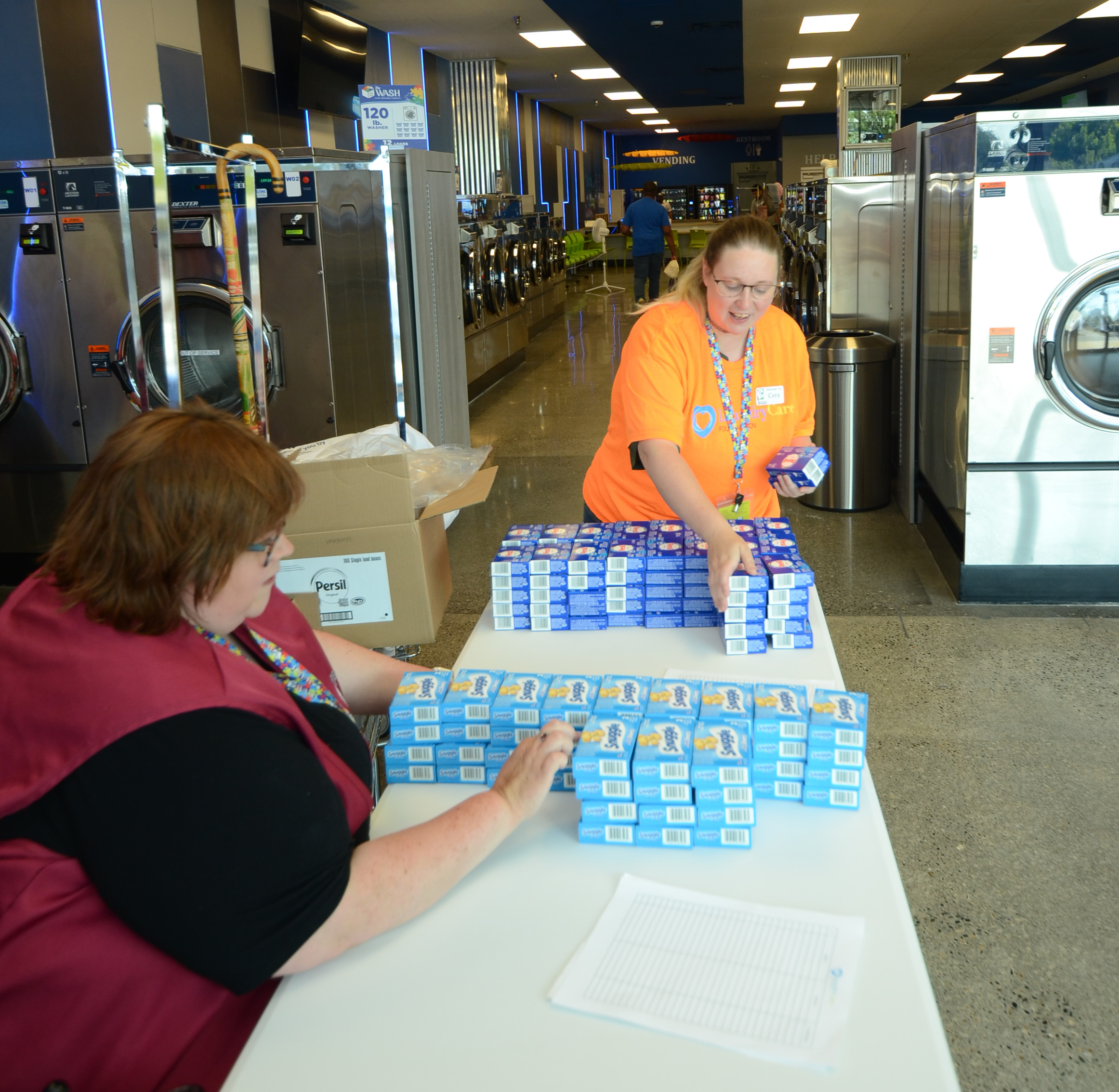 Volunteers welcoming visitors at a Free Laundry Day table inside The Wash